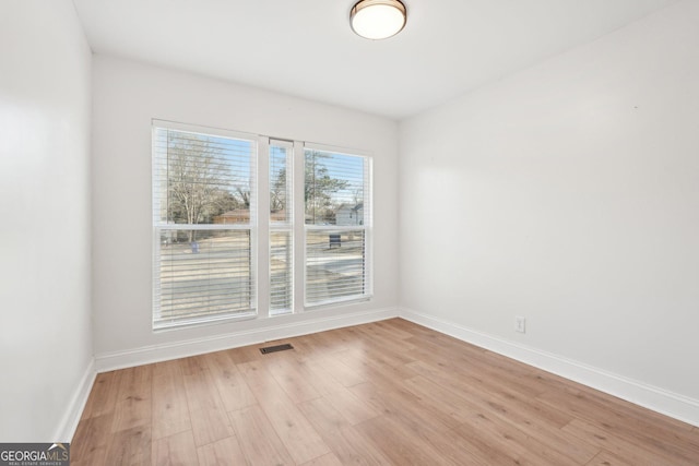 empty room with light wood finished floors, baseboards, and visible vents