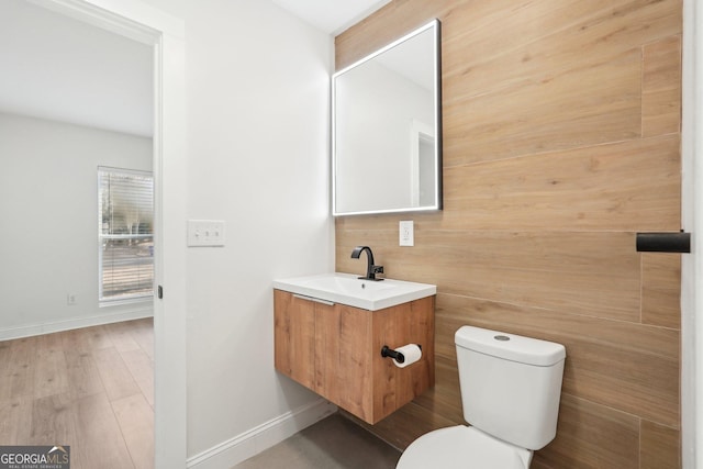 half bath with toilet, baseboards, wood finished floors, and vanity