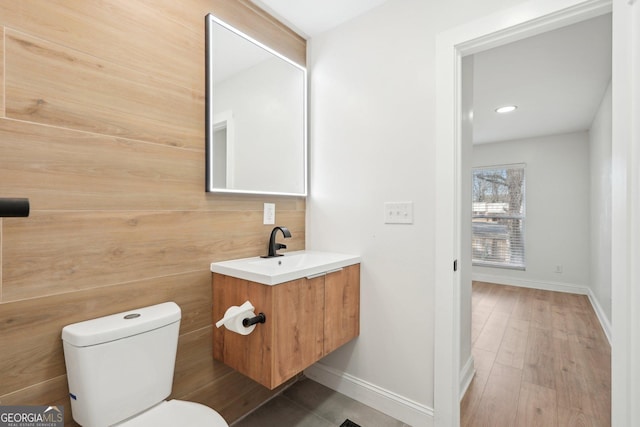 half bathroom with toilet, baseboards, wood finished floors, and vanity