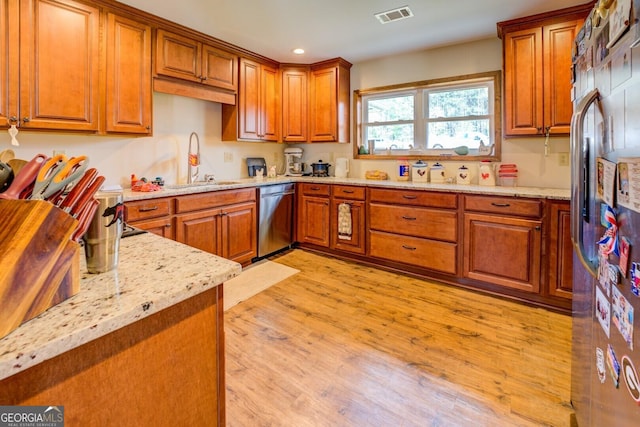 kitchen with light wood-type flooring, stainless steel appliances, light stone countertops, and sink