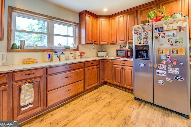 kitchen featuring light wood-type flooring, light stone counters, and stainless steel fridge with ice dispenser