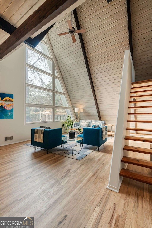 unfurnished living room featuring stairs, high vaulted ceiling, light wood-style flooring, and beam ceiling