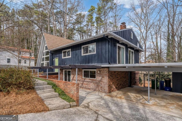 view of front facade with brick siding, a chimney, a shingled roof, board and batten siding, and an attached carport