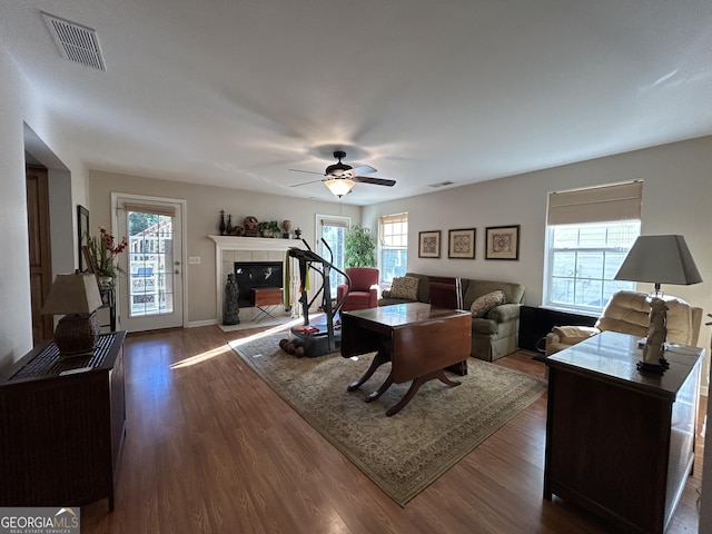 living area with dark wood-style flooring, visible vents, a fireplace, and ceiling fan