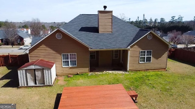 back of property with a yard, a wooden deck, and a storage shed