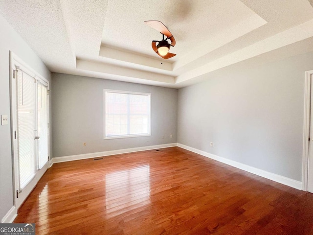 unfurnished bedroom featuring a tray ceiling, hardwood / wood-style floors, a textured ceiling, and ceiling fan