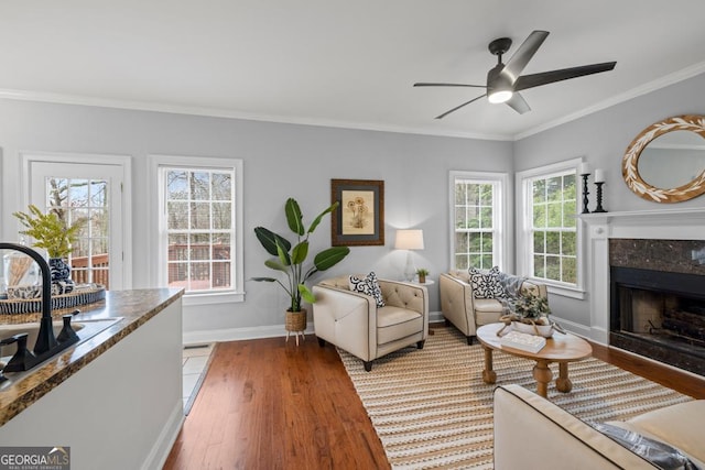 living area with crown molding, a high end fireplace, a ceiling fan, light wood finished floors, and baseboards