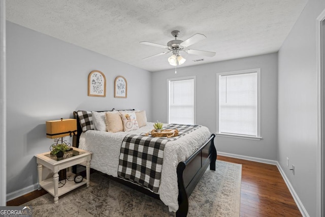 bedroom featuring baseboards, dark wood-style flooring, a textured ceiling, and visible vents