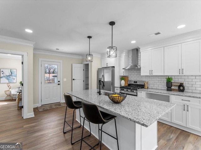 kitchen featuring wall chimney range hood, a center island with sink, white cabinetry, and stainless steel appliances