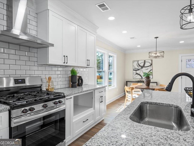 kitchen featuring decorative light fixtures, stainless steel range with gas stovetop, sink, white cabinets, and wall chimney exhaust hood