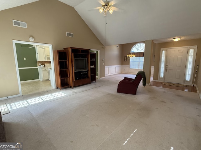 unfurnished living room with light carpet, high vaulted ceiling, ceiling fan with notable chandelier, and visible vents