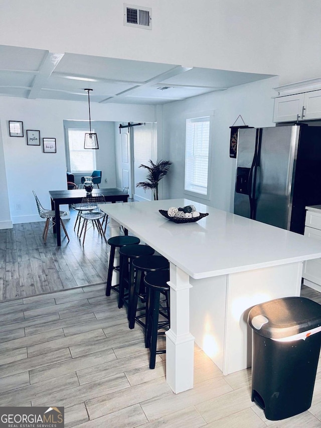 kitchen featuring stainless steel fridge with ice dispenser, a spacious island, hanging light fixtures, a barn door, and white cabinets