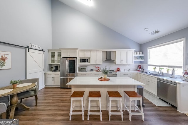 kitchen featuring stainless steel appliances, wall chimney range hood, a barn door, a kitchen island, and sink