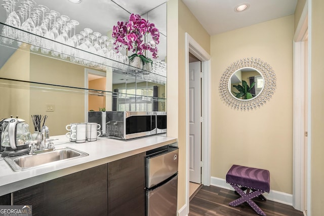 bar featuring dark wood-type flooring, baseboards, recessed lighting, stainless steel appliances, and a sink