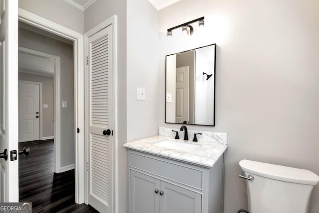 bathroom featuring baseboards, toilet, wood finished floors, crown molding, and vanity