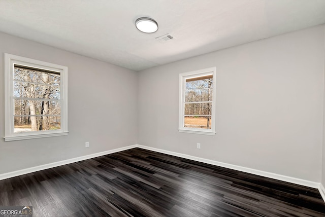 spare room with baseboards, visible vents, and dark wood finished floors