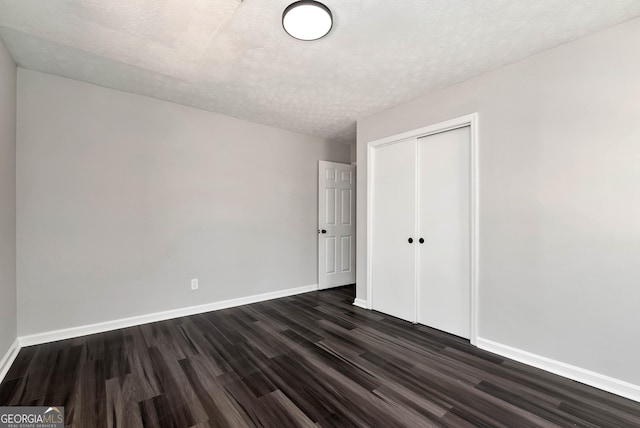 unfurnished bedroom featuring dark wood-type flooring, a closet, a textured ceiling, and baseboards