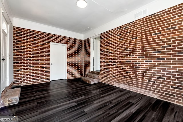 empty room featuring brick wall, dark wood-style flooring, and visible vents