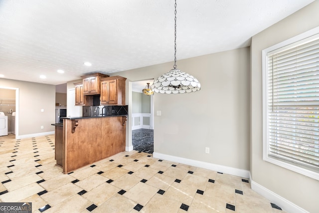 kitchen featuring a kitchen bar, pendant lighting, washer and clothes dryer, a textured ceiling, and kitchen peninsula