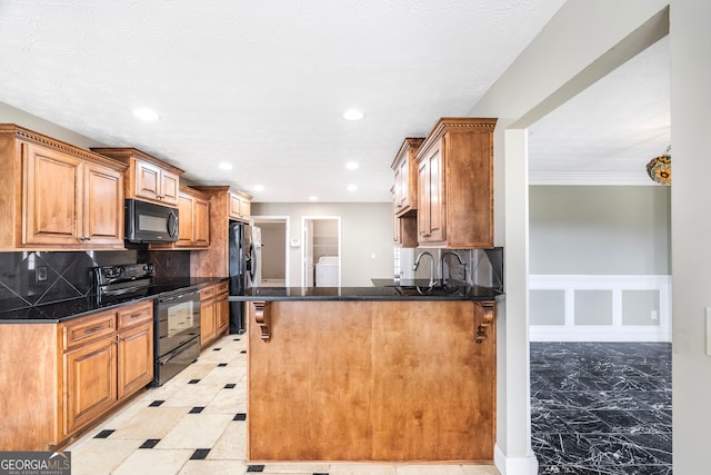 kitchen featuring black appliances, decorative backsplash, washing machine and dryer, sink, and kitchen peninsula