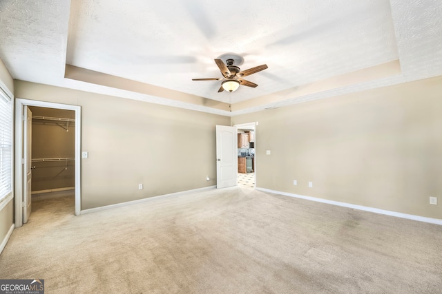 unfurnished bedroom featuring a raised ceiling, a textured ceiling, a walk in closet, and light colored carpet