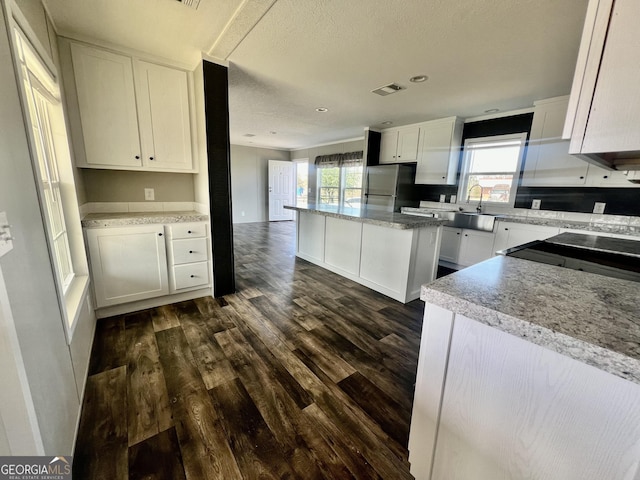 kitchen with white cabinets, stainless steel fridge, dark hardwood / wood-style flooring, and a center island