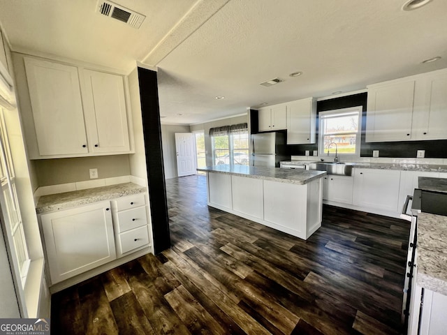 kitchen featuring a kitchen island, white cabinetry, light stone countertops, and stainless steel fridge