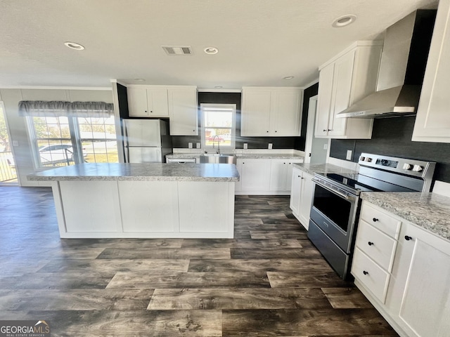 kitchen with stainless steel electric range oven, fridge, a kitchen island, wall chimney range hood, and white cabinets