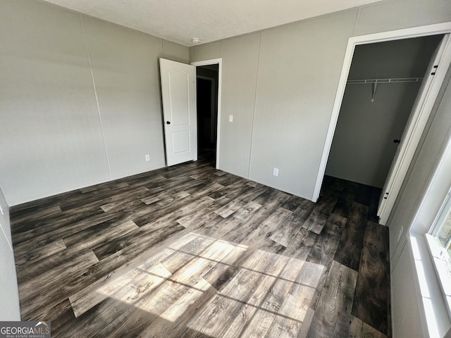 unfurnished bedroom with a walk in closet, a closet, and dark hardwood / wood-style flooring