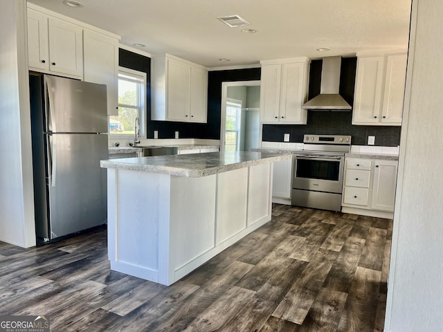 kitchen featuring appliances with stainless steel finishes, tasteful backsplash, white cabinets, wall chimney range hood, and dark hardwood / wood-style flooring