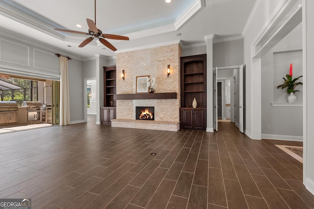 unfurnished living room with a tray ceiling, a stone fireplace, dark hardwood / wood-style floors, and built in shelves