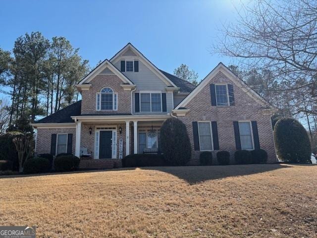 view of front of home with covered porch, brick siding, and a front yard