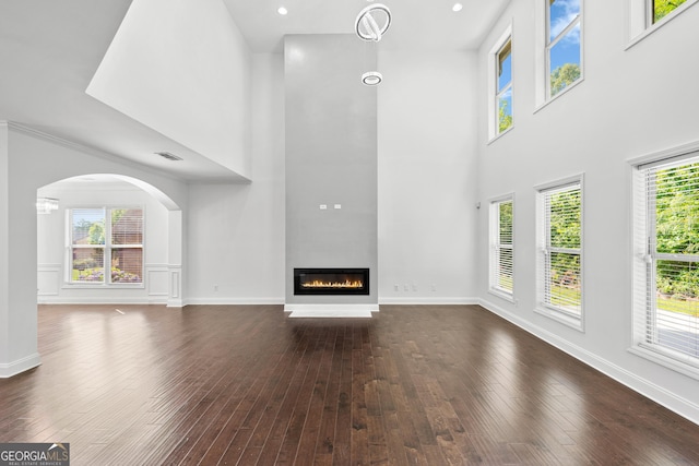 868 Still Hill Ln, Lawrenceville, GA 30045 - unfurnished living room featuring a high ceiling, dark wood-type flooring, a glass covered fireplace, and arched walkways
