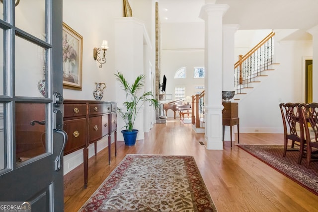 foyer entrance with decorative columns, a towering ceiling, and light wood-type flooring