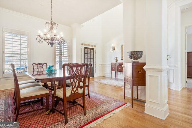 dining space featuring ornamental molding, light wood-type flooring, ornate columns, and an inviting chandelier