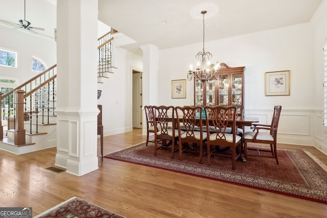 dining area with ceiling fan with notable chandelier, wood-type flooring, decorative columns, and ornamental molding