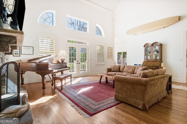 living room featuring hardwood / wood-style flooring, a stone fireplace, a high ceiling, and french doors