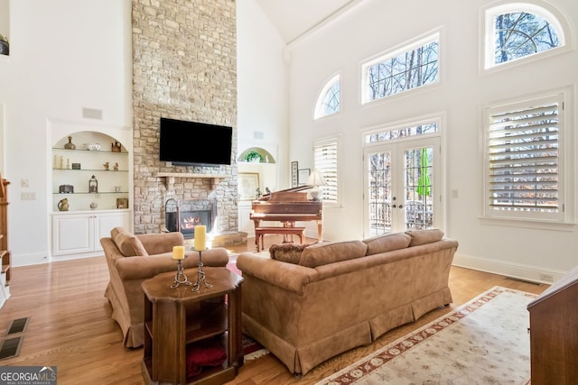 living room featuring french doors, built in shelves, light hardwood / wood-style flooring, a stone fireplace, and high vaulted ceiling