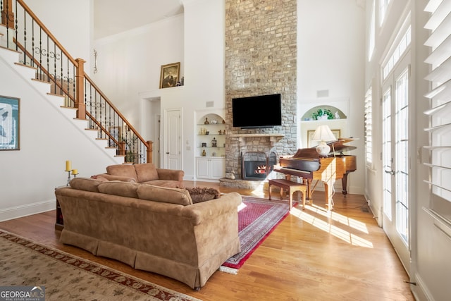 living room featuring a high ceiling, built in shelves, a stone fireplace, and wood-type flooring