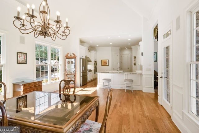 dining room with light wood-type flooring, high vaulted ceiling, sink, and an inviting chandelier