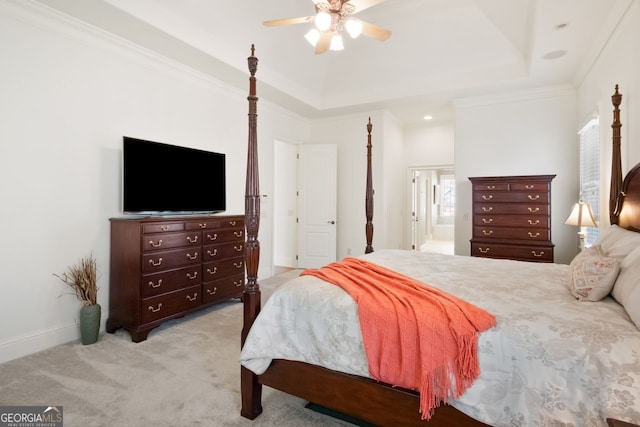 carpeted bedroom with a tray ceiling, ornamental molding, ensuite bathroom, and ceiling fan