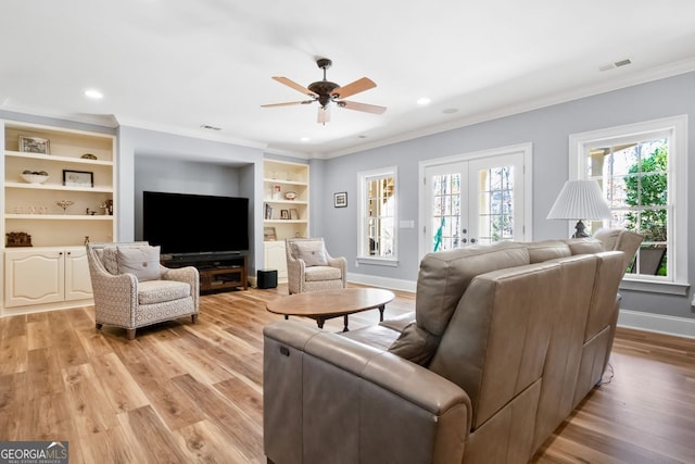 living room featuring built in features, french doors, crown molding, and light hardwood / wood-style floors