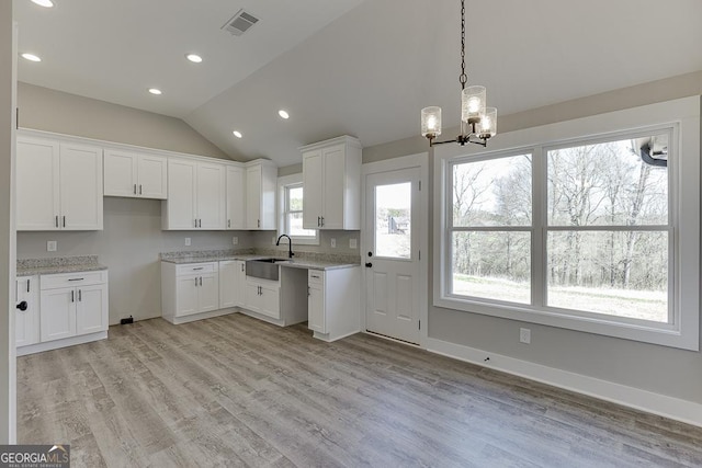 kitchen with hanging light fixtures, white cabinetry, vaulted ceiling, a sink, and light wood-type flooring