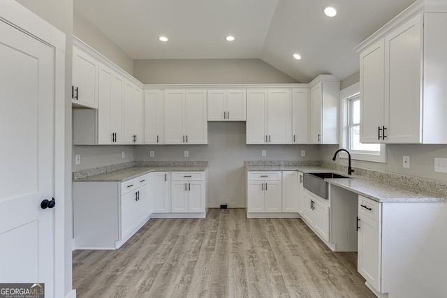 kitchen featuring light stone countertops, light wood-style flooring, white cabinets, and a sink