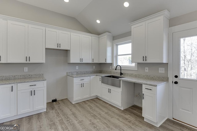 kitchen with lofted ceiling, light wood-style floors, a sink, and white cabinets