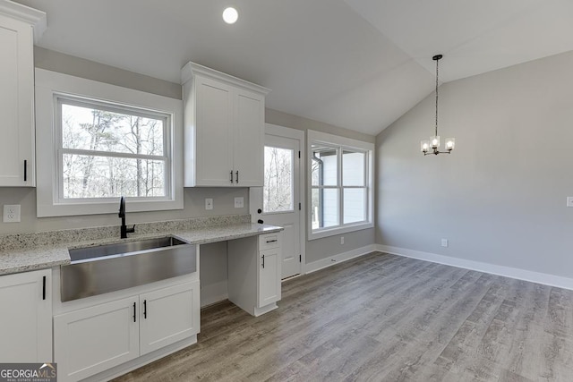 kitchen featuring plenty of natural light, lofted ceiling, light stone counters, white cabinetry, and a sink