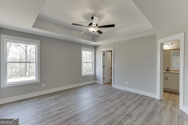 unfurnished bedroom featuring light wood finished floors, visible vents, baseboards, and a raised ceiling