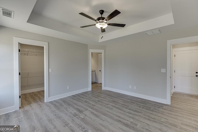 unfurnished bedroom with light wood-style flooring, visible vents, a raised ceiling, and baseboards