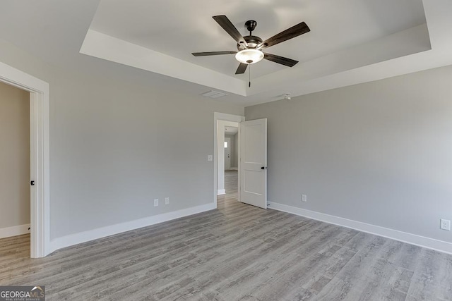 spare room featuring light wood-style floors, baseboards, a tray ceiling, and ceiling fan