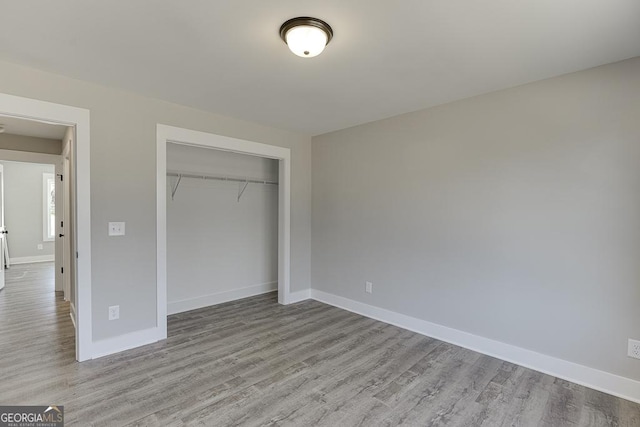 unfurnished bedroom featuring light wood-type flooring, a closet, and baseboards